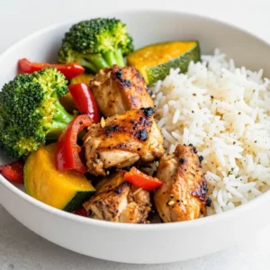 A sheet pan filled with roasted chicken thighs and colorful vegetables like carrots, zucchini, and bell peppers.