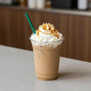 A chilled pumpkin spice iced latte in a clear glass with ice cubes, whipped cream, and a sprinkle of cinnamon on top.
